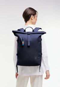 Zaino roll-top navy con spallacci regolabili, tasca frontale con zip e dettaglio del logo. Realizzato in materiale resistente con una finitura liscia.