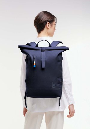 La mochila roll-top navy cuenta con un material impermeable, correas ajustables, un bolsillo lateral y un llavero decorativo con acentos de color.