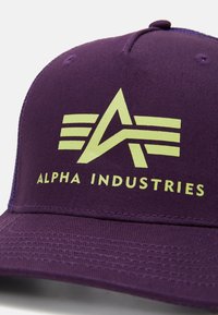 Casquette de baseball violette Alpha Industries avec logo jaune et texte à l'avant, montrant une lettre A stylisée avec trois bandes horizontales.