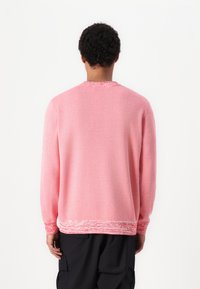 Genser i lys rosa strikk med teksturerte mansjetter og kant, med et mønsterdetalj. Klassisk rund hals og lange ermer.