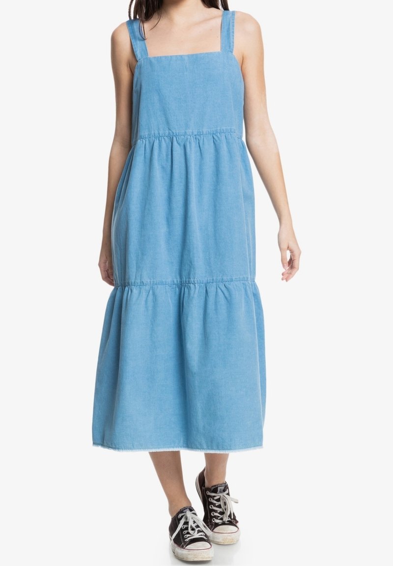 Lichtblauwe denimjurk met brede bandjes, een aansluitend lijfje en een geplooide, gelaagde rok; afgewerkt met een zoom met rafelige randen.