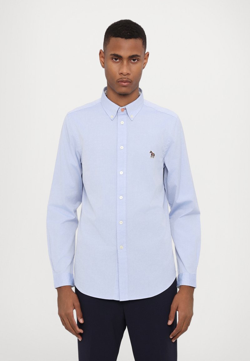 Chemise à manches longues bleu clair avec col boutonné, boutons sur le devant et petit logo brodé. Fabriquée en tissu tissé avec une texture lisse.