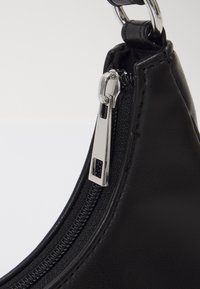 Černá kožená kabelka s texturovaným povrchem, vybavená stříbrným zipem a táhlem, šikmým designem a kulatým kovovým akcentem.