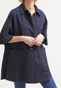 Námořnická modrá oversized bunda s límečkem, zapínáním na knoflíky a dvěma předními kapsami; vyrobená z texturované látky.
