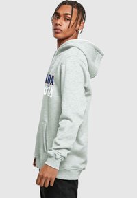 Sudadera gris con bolsillo frontal, texto bordado en azul y blanco, presenta puños y dobladillo de canalé, fabricada en material de forro polar suave.