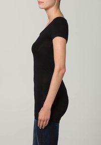 Fekete, rövid ujjú, testhezálló póló, puha, rugalmas anyagból készült. A dizájn kör alakú nyakkivágással és sima felülettel rendelkezik.