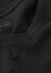 Czarna bawełniana koszulka o gładkiej fakturze, z prążkowanym dekoltem i widocznymi detalami zszycia. Bez wzorów ani grafik.