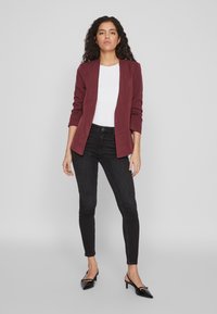 Bordowa marynarka o dopasowanym kroju, połączona z dopasowanymi czarnymi jeansami i czarnymi szpilkami z ostrym noskiem. Czyste linie i minimalistyczny styl.