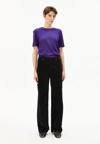 Paarse T-shirt met korte mouwen gecombineerd met zwart hoge taille wijde corduroy broek, voorzien van voorzakken en een knoopsluiting.