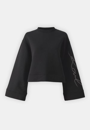 Schwarzer, gekürzter Sweatshirt aus weichem Stoff. Mit weiten Ärmeln und einem hohen Kragen, verziert mit einem silbernen Strassstein auf einem Ärmel.