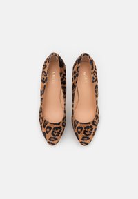 Pumps kuviolla leopardi, joissa on keinonahka, pyöristetty kärki ja sileä beige sisäpohja. Esittelee mustia yksityiskohtia kuviosta.