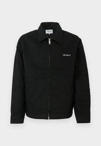 Μαύρο μπουφάν κατασκευασμένο από ανθεκτικό ύφασμα, με φερμουάρ μπροστά, κομμένο γιακά και ένα μικρό λευκό λογότυπο στο στήθος. Σχεδίαση ευθείας γραμμής.