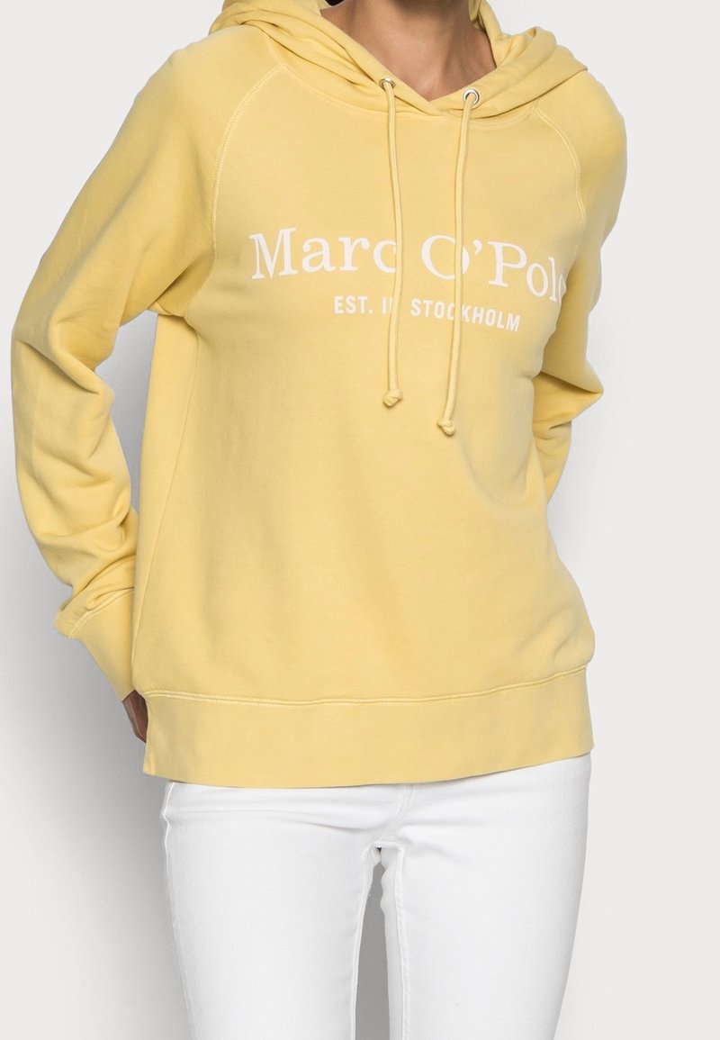 Sweat à capuche jaune en coton doux avec texte blanc "Marc O'Polo EST. À STOCKHOLM." Comprend un cordon de serrage ainsi que des poignets et un ourlet côtelés.