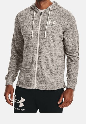 Homme portant un sweat à capuche zippé gris clair chiné avec des cordons blancs et un pantalon noir avec le logo blanc Under Armour sur la cuisse gauche.