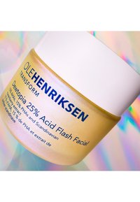 Żółty szklany słoik z białą pokrywką, oznaczony etykietą "OLEHENRIKSEN Dewtopia 25% Acid Flash Facial." Posiada błyszczącą teksturę i wyraźny niebieski tekst.