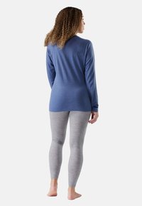 Maglietta blu a maniche lunghe con orlo arrotondato, abbinata a leggings grigi chiari con una sottile trama. Piedi nudi visibili.