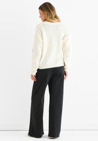 White knitted sweater with long sleeves and a loose fit, paired with black wide-leg jeans. The sweater features a textured pattern.