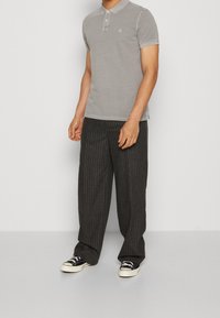 Grå polo med krage och tre knappar, kombinerad med svarta byxor med smalrand och vida ben samt svarta sneakers.