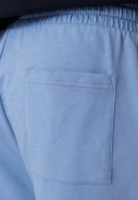 Világoskék pamut jogger nadrág elasztikus derékkal és négyzet alakú hátsó zsebbel, amely látható varrási részletekkel rendelkezik.