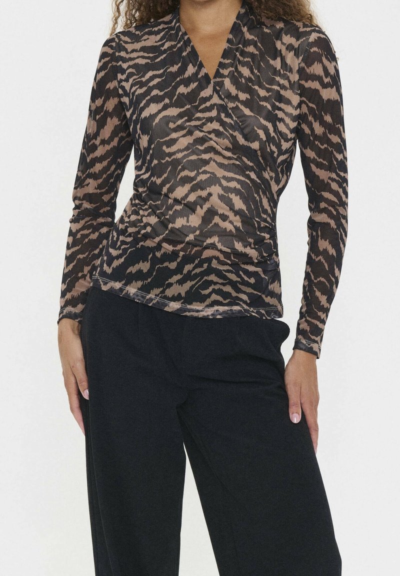 Femme portant un haut cache-cœur à manches longues imprimé tigre et un pantalon noir, les mains reposant le long du corps sur un fond blanc uni.