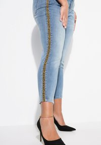 Jeans de mezclilla en azul claro con una franja de estampado de leopardo a lo largo del lateral. Diseño ajustado con una longitud recortada y combinados con tacones altos negros.