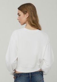 Felpa bianca corta con maniche lunghe e larghe e collo a costine, abbinata a jeans blu a vita alta.