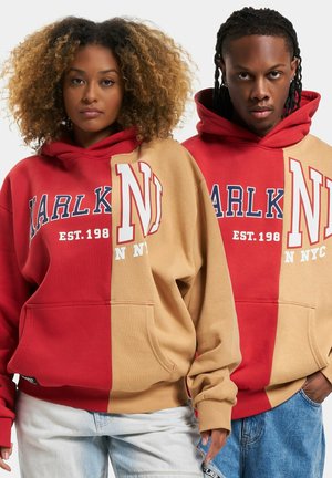 Hoodies in red and tan with a split design. Features a front kangaroo pocket, ribbed cuffs, and large logo text in contrasting colors.