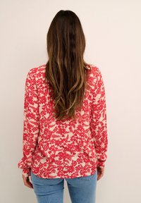 Top a maniche lunghe con una stampa floreale rossa e bianca, realizzato in tessuto leggero con una vestibilità rilassata e un orlo leggermente curvo.