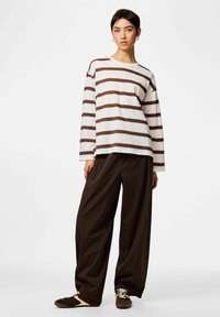 Valge ja pruuni triibulise pika varrukaga särk, koos lahtiste, tumepruuni triibuliste pükstega ja pruunide vabaajajalatsitega.