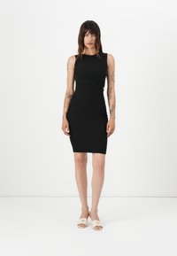 Musta bodycon-mekko, jossa on olkaimeton muotoilu ja kaarisaumadetaali. Yhdistetty vaaleanbeigeihin liukuviin sandaaleihin, joissa on kolmion muotoinen yksityiskohta.