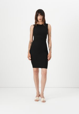 Svart bodycon-kjole med ermeløs design og buet sømdetalj. Kombinert med lysebeige sklisandaler med en trekantet aksent.