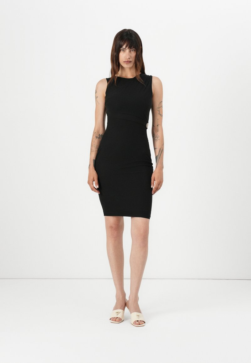 Musta bodycon-mekko, jossa on olkaimeton muotoilu ja kaarisaumadetaali. Yhdistetty vaaleanbeigeihin liukuviin sandaaleihin, joissa on kolmion muotoinen yksityiskohta.