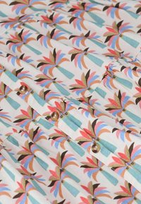 Ein blumengeprägter Stoff mit stilisierten Blättern in Pink, Blau und Grün auf weißem Hintergrund, verziert mit kleinen braunen Knöpfen und strukturierten Details.