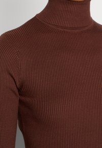 Brun ribbad polotröja med en åtsittande design, som har en texturerad yta och hög krage. Tyget är slätt med en lätt stretch.