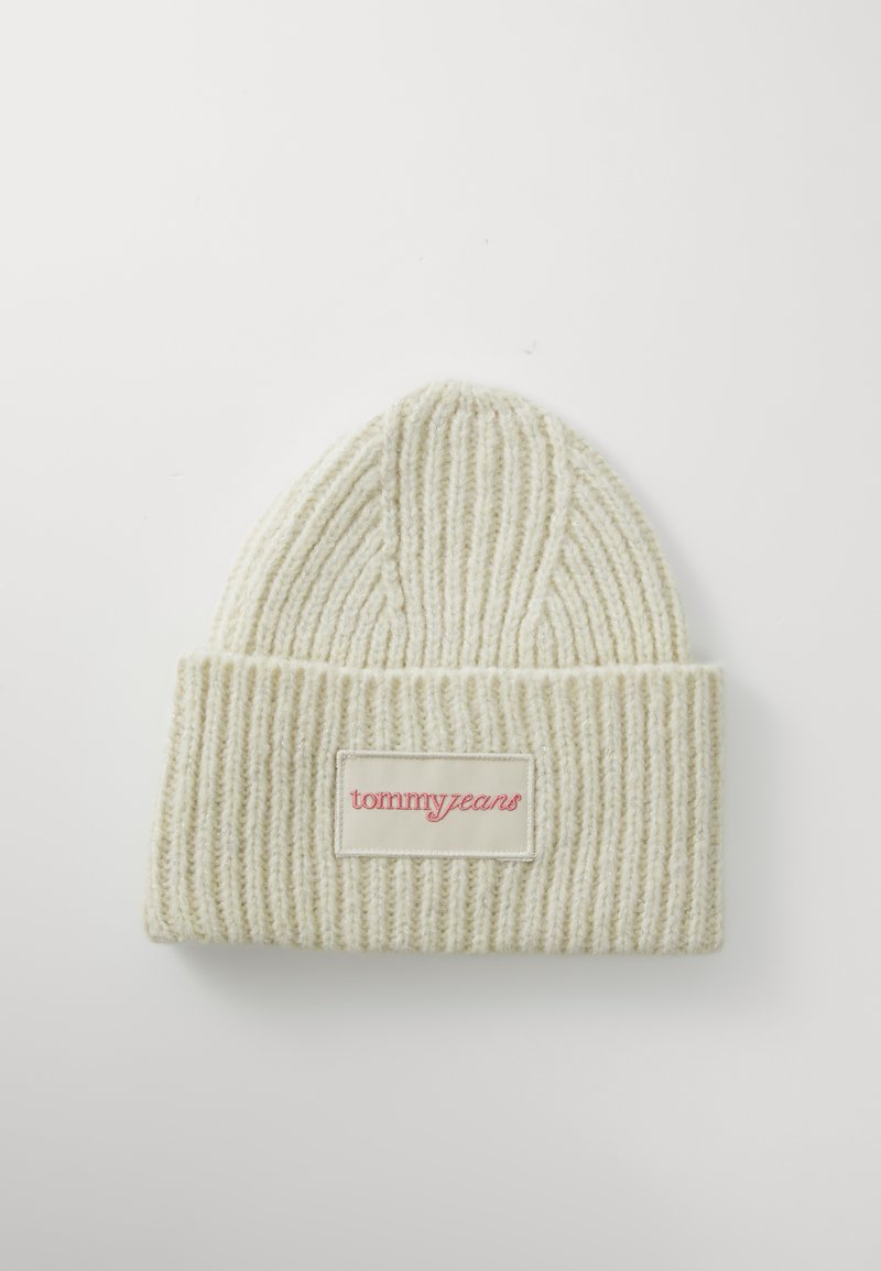 Bonnet en tricot de couleur crème avec des côtes verticales, présentant un revers repliable et un patch rectangulaire blanc avec le logo rouge "tommy jeans".