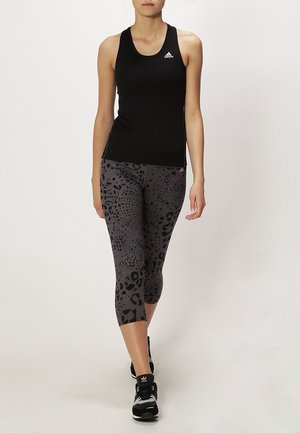 Mujer caminando con una blusa negra sin mangas, leggings capri de estampado de leopardo gris y zapatillas deportivas negras.