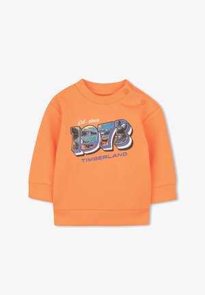 Sweat-shirt en coton orange avec poignets et col côtelés. Présente un graphisme "1973" et "Timberland" en bleu et blanc. Détails de boutons pression à l'épaule.