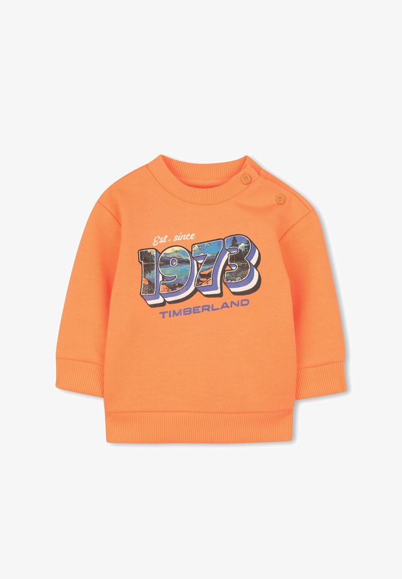 Sweat-shirt en coton orange avec poignets et col côtelés. Présente un graphisme "1973" et "Timberland" en bleu et blanc. Détails de boutons pression à l'épaule.