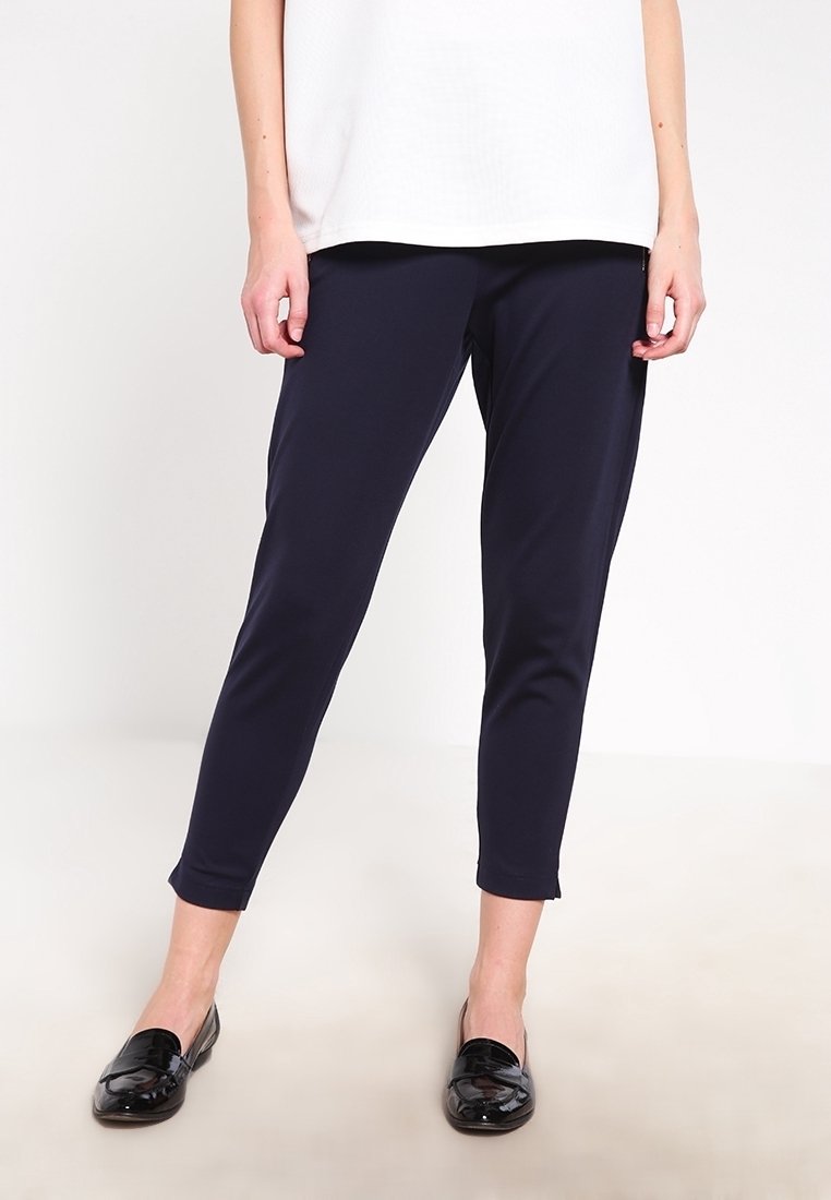 Navy blue tapered trousers in a smooth, stretch fabric with an elastic waistband, paired with black patent loafers.