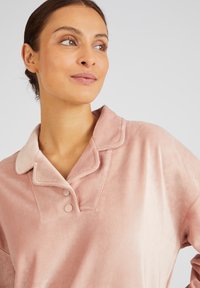 Top de pana rosa con cuello, que presenta dos botones y una textura suave, mostrando un ligero degradado de claro a oscuro.