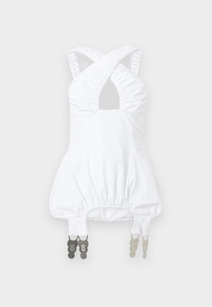 Bela brezrokavka z nabrano trakovi, ki se križajo na prsih, napihnjenim pasom in nastavljivimi kovinskimi zaponkami, ki visijo na robu.