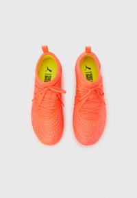 Lyseorange sportssko med en struktureret overdel, der har prikkede mønstre, snørebånd og en gul indersål med et logo.