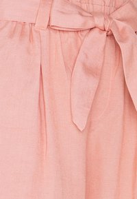 Tejido de color rosa claro con una textura suave, que presenta plisados y un detalle de cintura atada. El diseño es simple con un acabado liso.