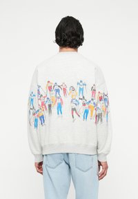 Szara bluza z obrazkiem narciarzy w różnych kolorowych strojach na plecach. Luźny krój, ściągacze przy mankietach i u dołu.