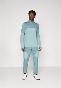 Svetlomodrý športový outfit pozostávajúci z dlhého rukávu s polozipom a zúžených nohavíc s kontrastnými svetlomodrými akcentmi a detailom loga.