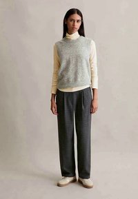 Maglione senza maniche grigio chiaro sopra un dolce vita crema, abbinato a pantaloni larghi a quadri neri e grigi, e sneakers crema.
