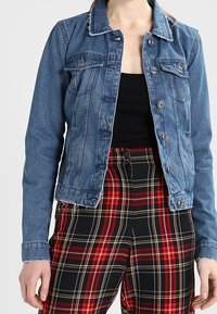 Denimjacka med en skräddarsydd design, blå färg, knappstängningar, två bröstfickor och fransad nederkant. Matchad med röd och svart rutiga byxor.