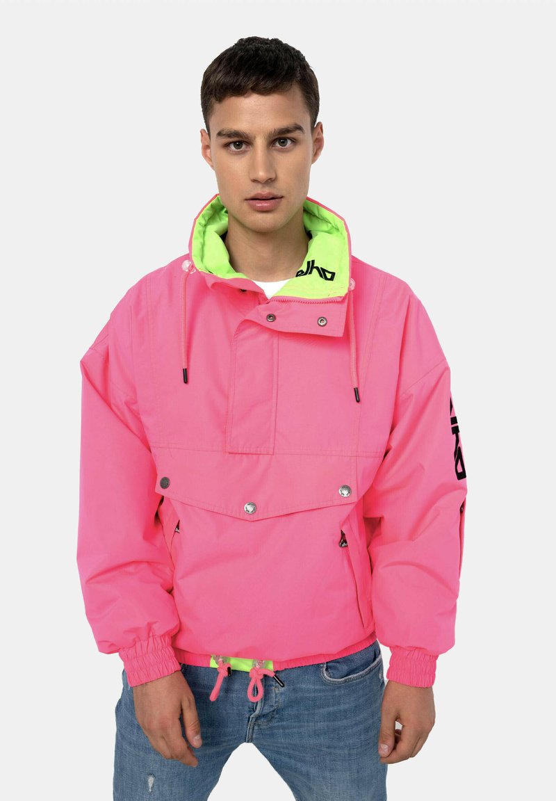 Rosa übergroße Jacke mit einer neon-grünen Kapuze, verstellbaren Kordeln, Druckknöpfen und einer vorderen Klapptasche. Text auf dem Ärmel.