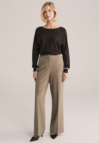 Fekete hosszú ujjú felső és taupe színű bő szárú nadrág. A nadrág elöl redőzött és sima textúrájú, sötét hegyes orrú cipővel párosítva.