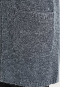 Grå ullig plagg med en mjuk, texturerad yta, som har två framfickor och ribbade kanter för en tät passform.